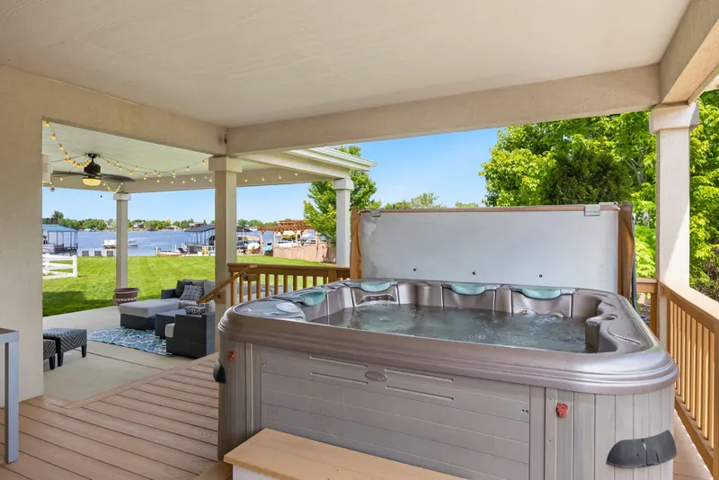 Explore a serene outdoor patio featuring a luxurious hot tub overlooking a tranquil lake